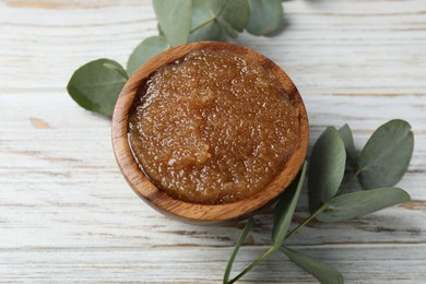 Photo of Natural body scrub in bowl and eucalyptus branches on wooden table, above view
