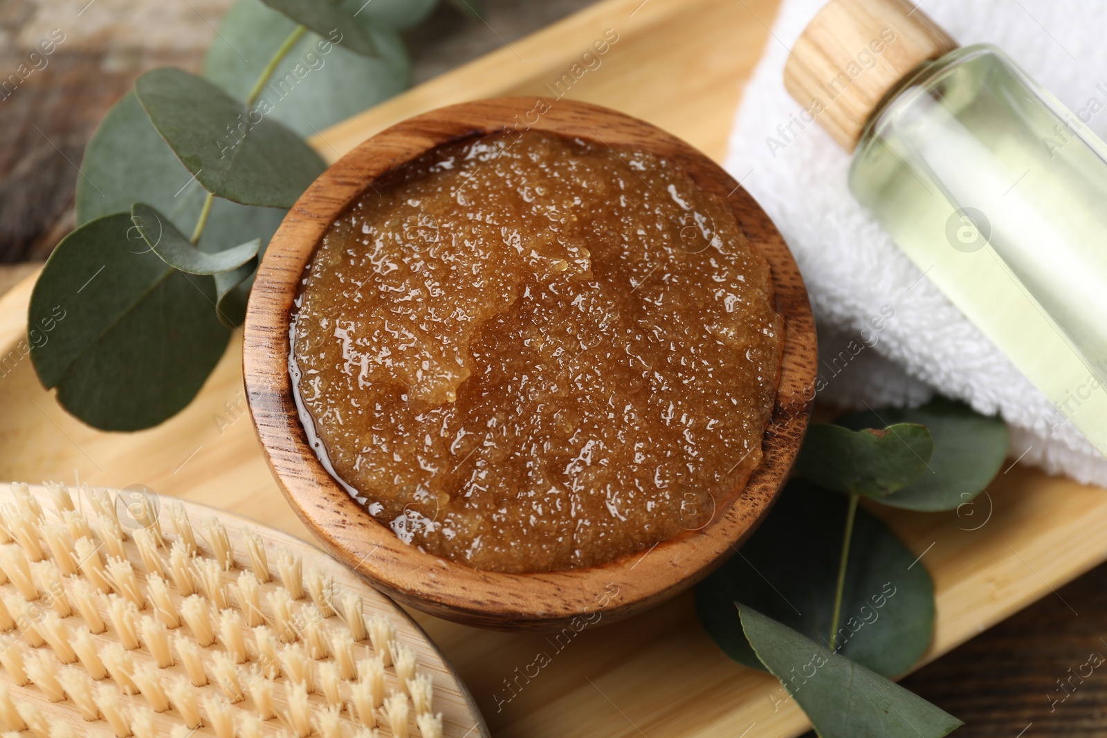 Photo of Natural body scrub in bowl, brush, essential oil, towel and eucalyptus branches on table, above view
