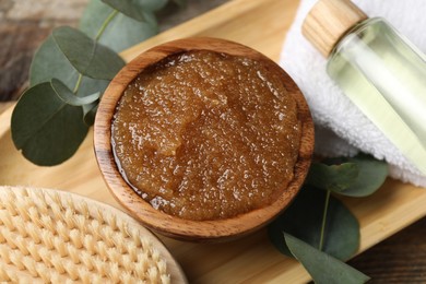Photo of Natural body scrub in bowl, brush, essential oil, towel and eucalyptus branches on table, above view