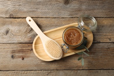 Photo of Natural body scrub in glass jar, brush and eucalyptus branch on wooden table, top view
