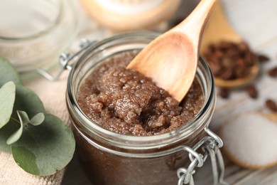 Photo of Natural body scrub in glass jar, spoon and ingredients on table, closeup