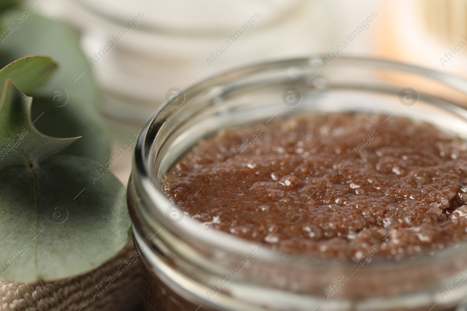 Natural body scrub in glass jar, eucalyptus leaves and towel on blurred background, closeup Photo of Natural body scrub in glass jar, eucalyptus leaves and towel on blurred background, closeup