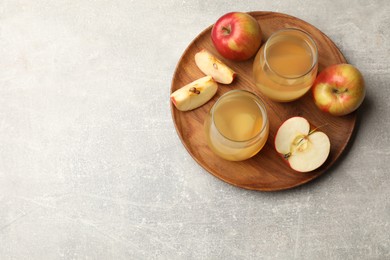Photo of Tasty compot in glasses and fresh apples on grey table, top view. Space for text
