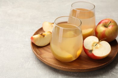 Photo of Tasty compot in glasses and fresh apples on grey table, closeup. Space for text