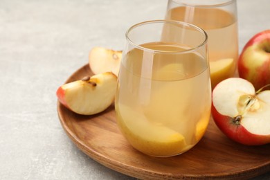 Photo of Tasty compot in glasses and fresh apples on grey table, closeup
