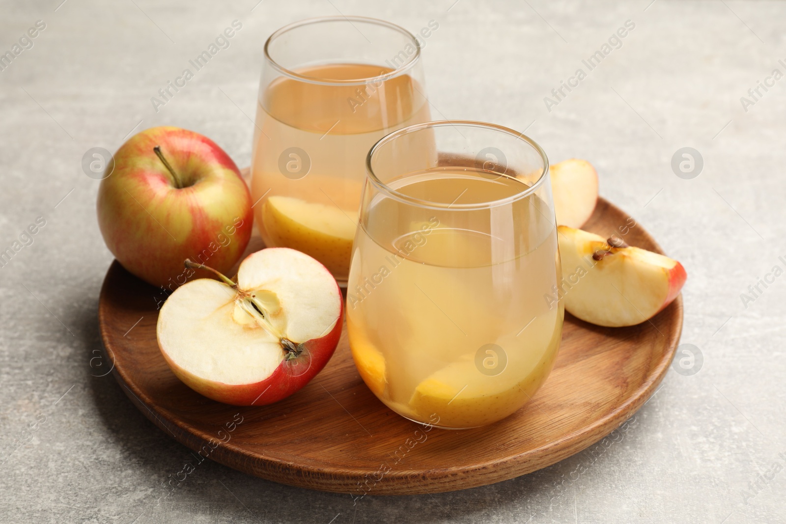 Photo of Tasty compot in glasses and fresh apples on grey table, closeup