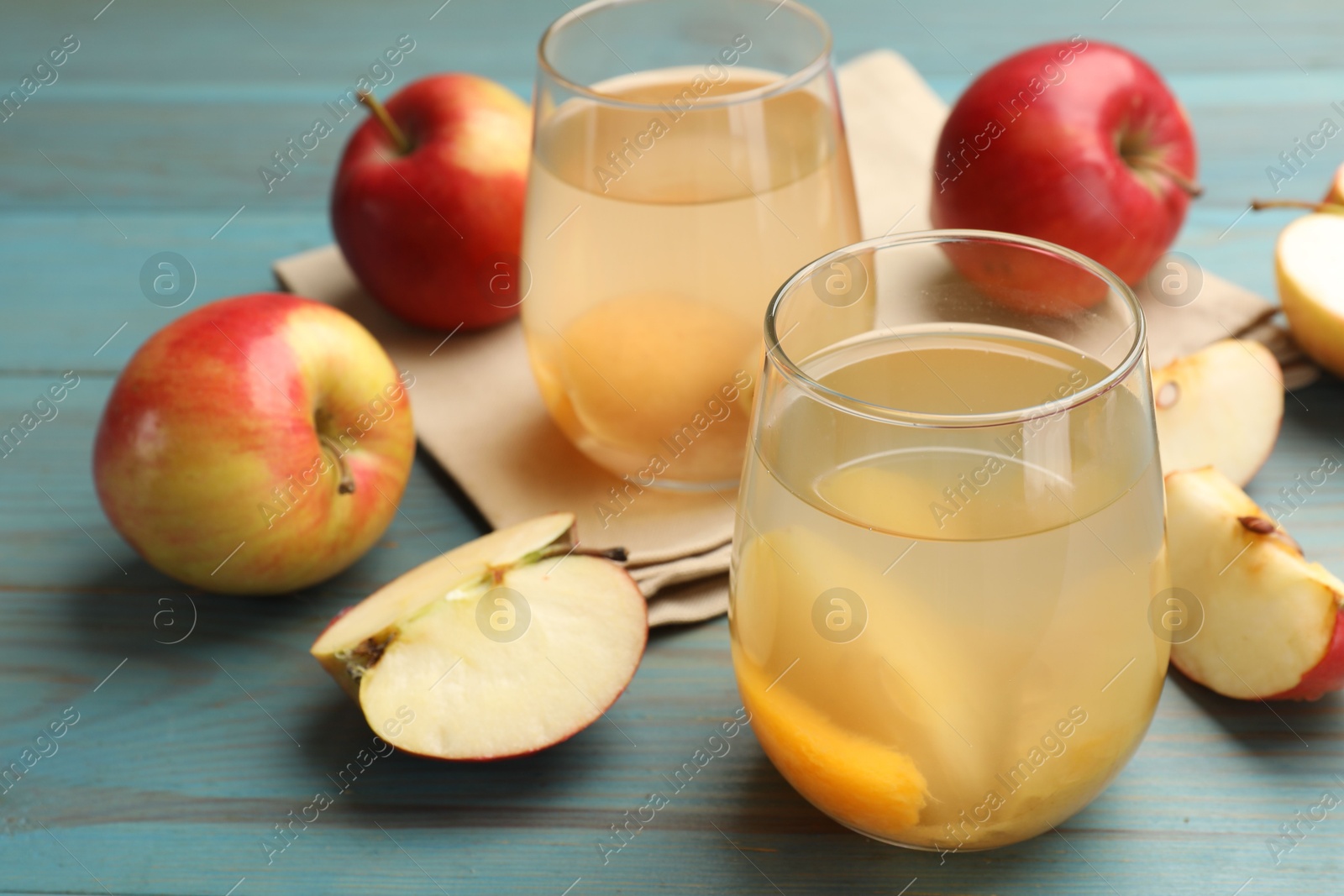 Photo of Tasty compot in glasses and fresh apples on light blue wooden table, closeup