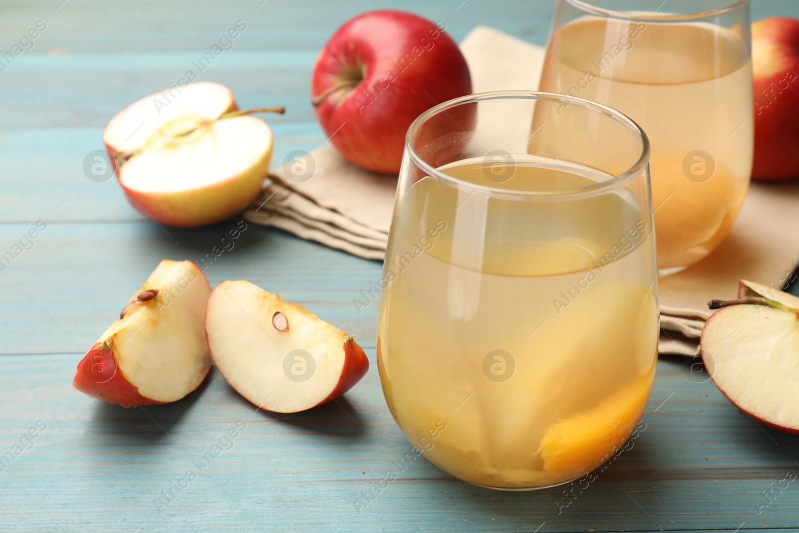 Photo of Tasty compot in glasses and fresh apples on light blue wooden table, closeup