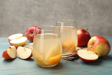 Photo of Tasty compot in glasses and fresh apples on light blue wooden table