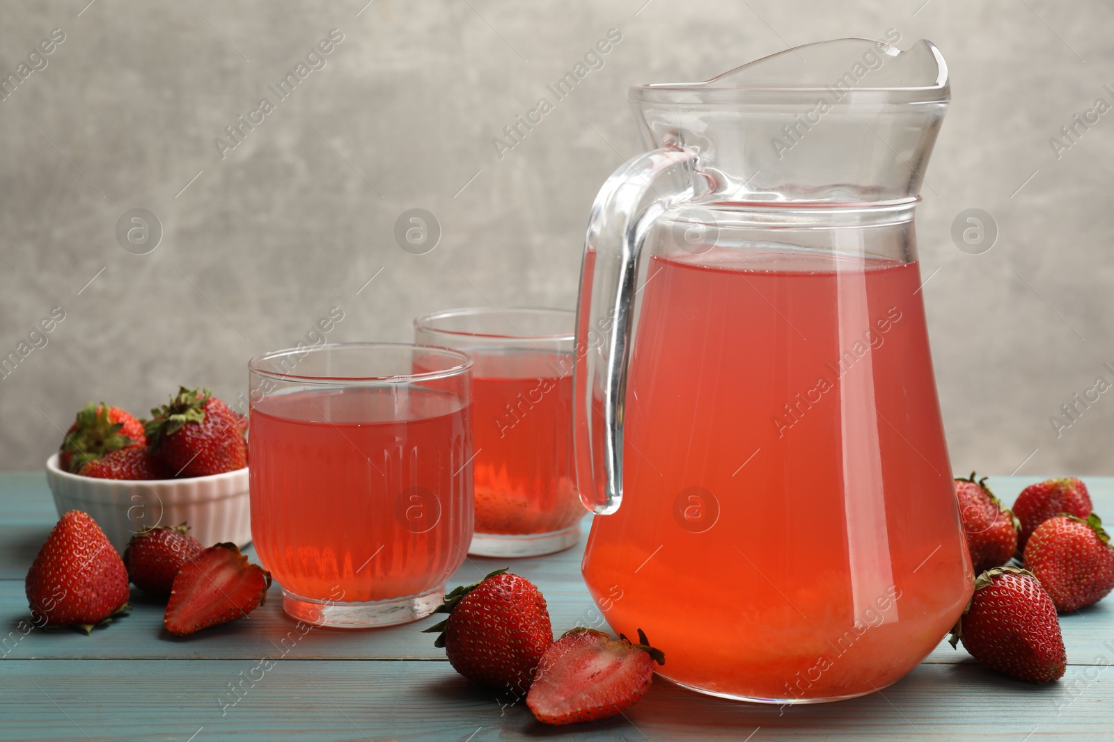 Photo of Tasty compot in glasses, jug and fresh strawberries on light blue wooden table, closeup