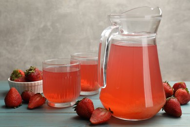 Photo of Tasty compot in glasses, jug and fresh strawberries on light blue wooden table, closeup