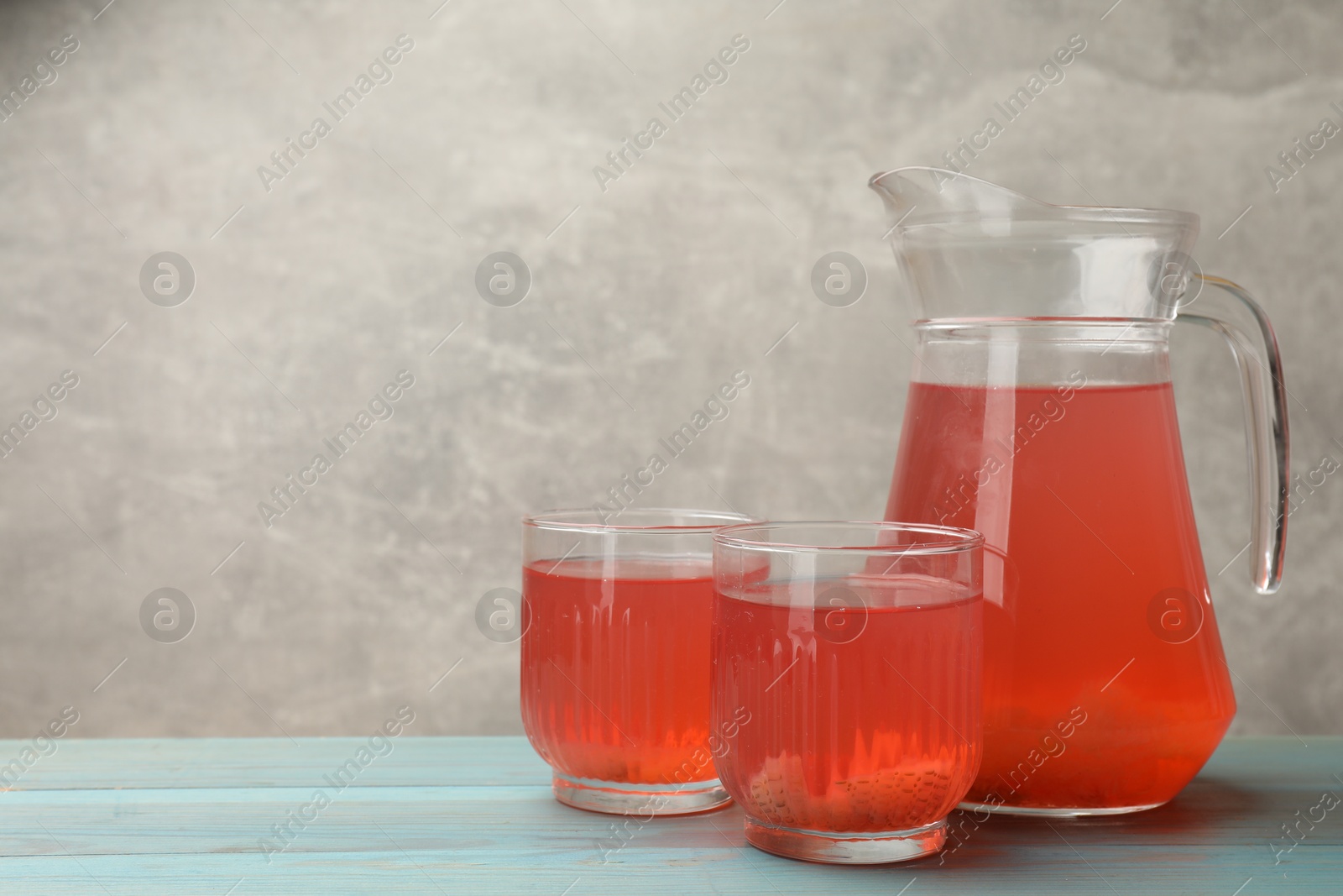 Photo of Tasty compot in glasses and jug on light blue wooden table, space for text