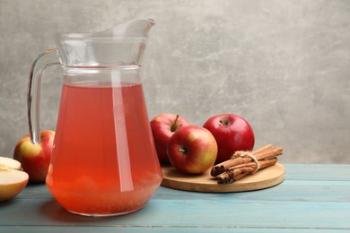 Photo of Tasty compot in glass jug, fresh apples and cinnamon on light blue wooden table