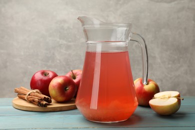 Photo of Tasty compot in glass jug, fresh apples and cinnamon on light blue wooden table
