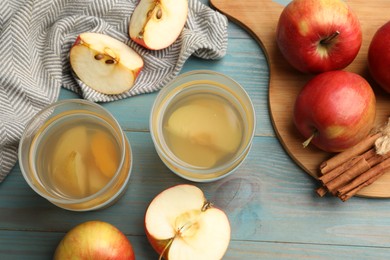 Photo of Tasty compot in glasses, fresh apples and cinnamon on light blue wooden table, flat lay