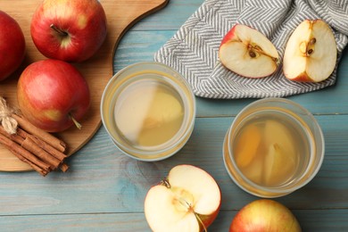 Photo of Tasty compot in glasses, fresh apples and cinnamon on light blue wooden table, flat lay