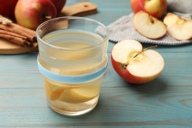 Photo of Tasty compot in glass, fresh apples and cinnamon on light blue wooden table, closeup