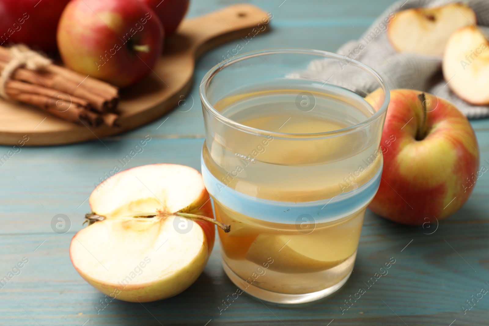Photo of Tasty compot in glass, fresh apples and cinnamon on light blue wooden table, closeup