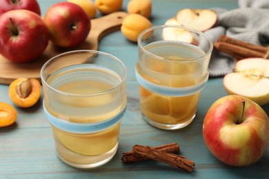 Photo of Tasty compot in glasses, fresh apples, apricots and cinnamon on light blue wooden table, closeup