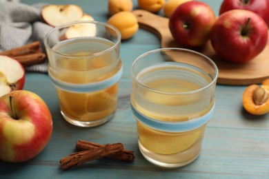 Photo of Tasty compot in glasses, fresh apples, apricots and cinnamon on light blue wooden table, closeup