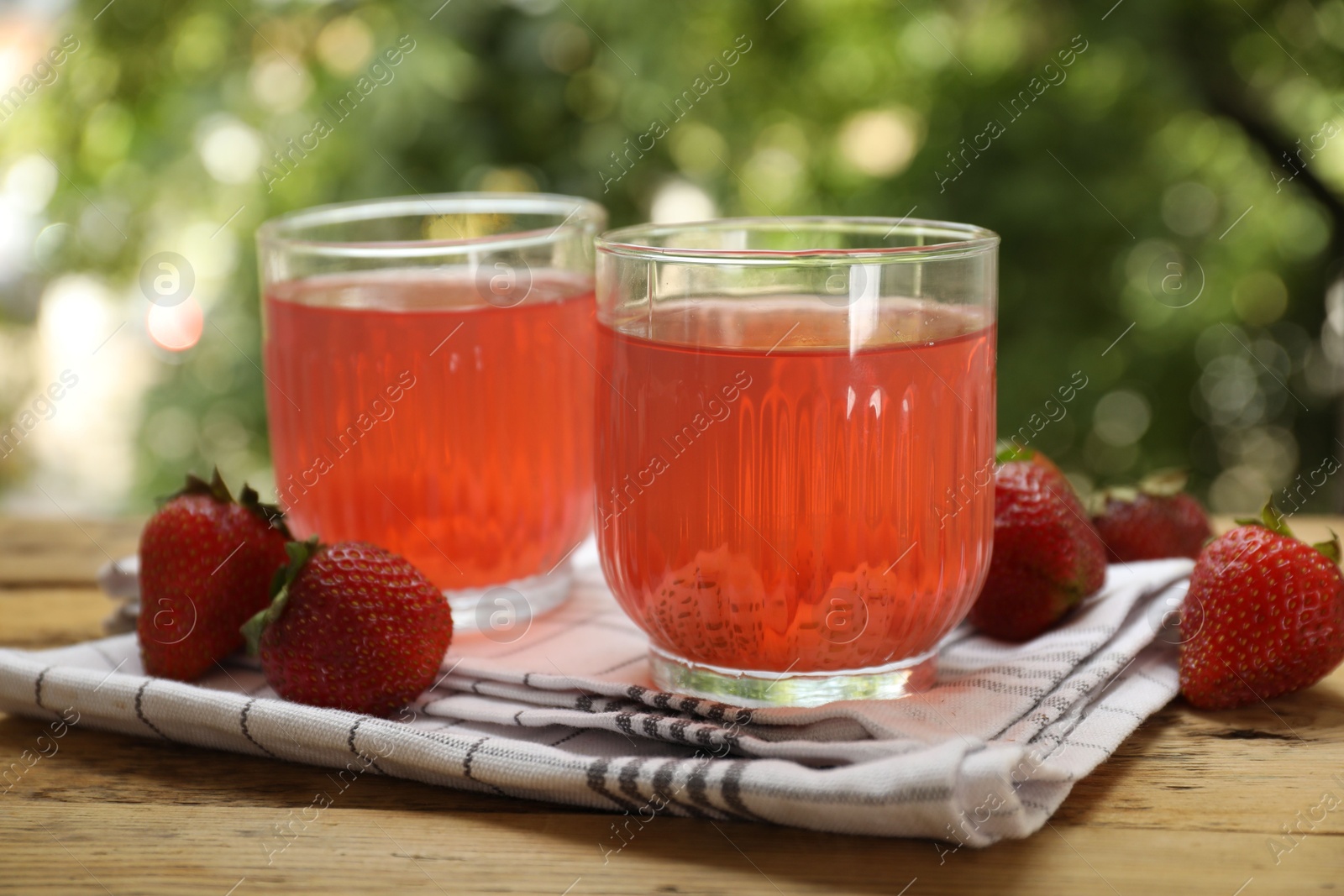 Photo of Tasty compot in glasses and fresh strawberries on wooden table outdoors, closeup