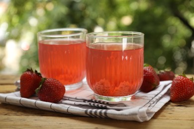 Photo of Tasty compot in glasses and fresh strawberries on wooden table outdoors, closeup