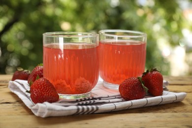 Photo of Tasty compot in glasses and fresh strawberries on wooden table outdoors, closeup