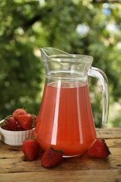Photo of Tasty compot in glass jug and fresh strawberries on wooden table outdoors