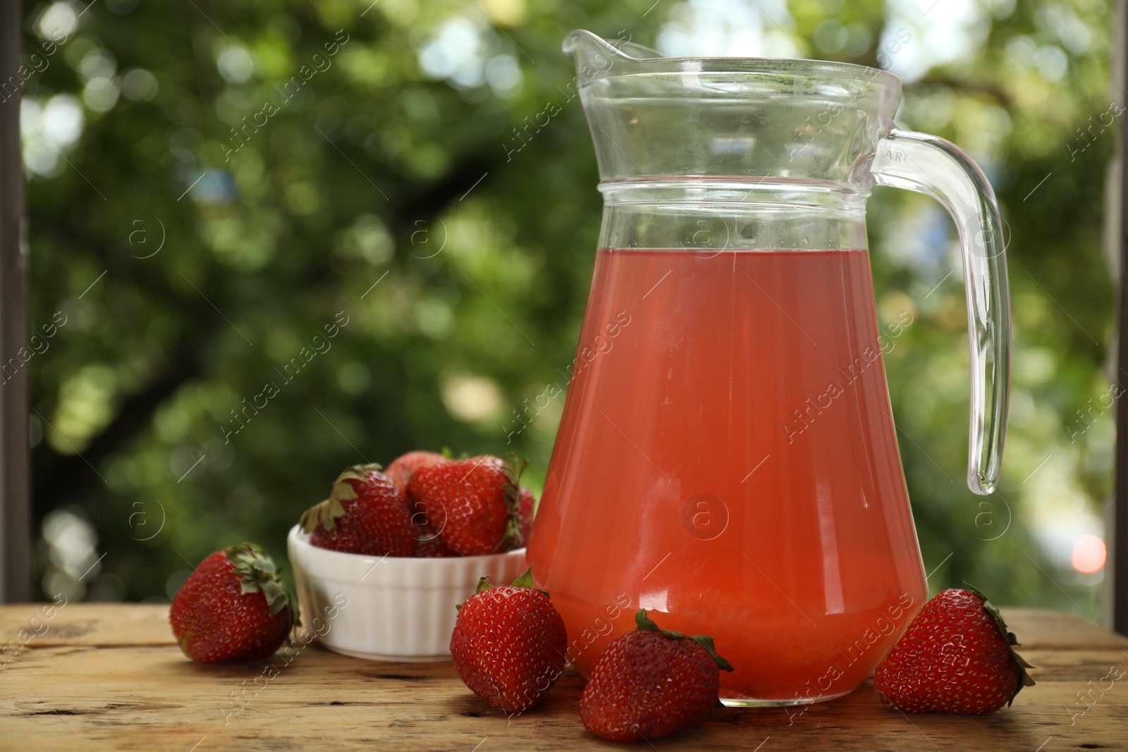 Photo of Tasty compot in glass jug and fresh strawberries on wooden table outdoors, closeup
