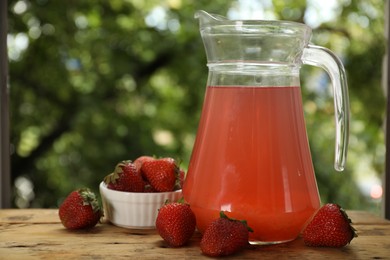 Photo of Tasty compot in glass jug and fresh strawberries on wooden table outdoors, closeup