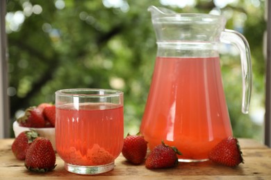 Photo of Tasty compot in glass, jug and fresh strawberries on wooden table outdoors, closeup
