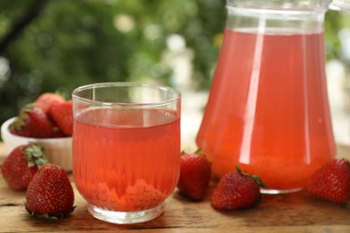 Photo of Tasty compot in glass, jug and fresh strawberries on wooden table outdoors, closeup