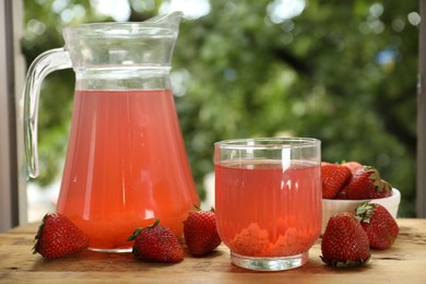 Photo of Tasty compot in glass, jug and fresh strawberries on wooden table outdoors