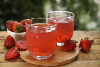 Photo of Tasty compot in glasses and fresh strawberries on wooden table outdoors, closeup