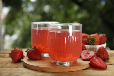 Photo of Tasty compot in glasses and fresh strawberries on wooden table outdoors, closeup