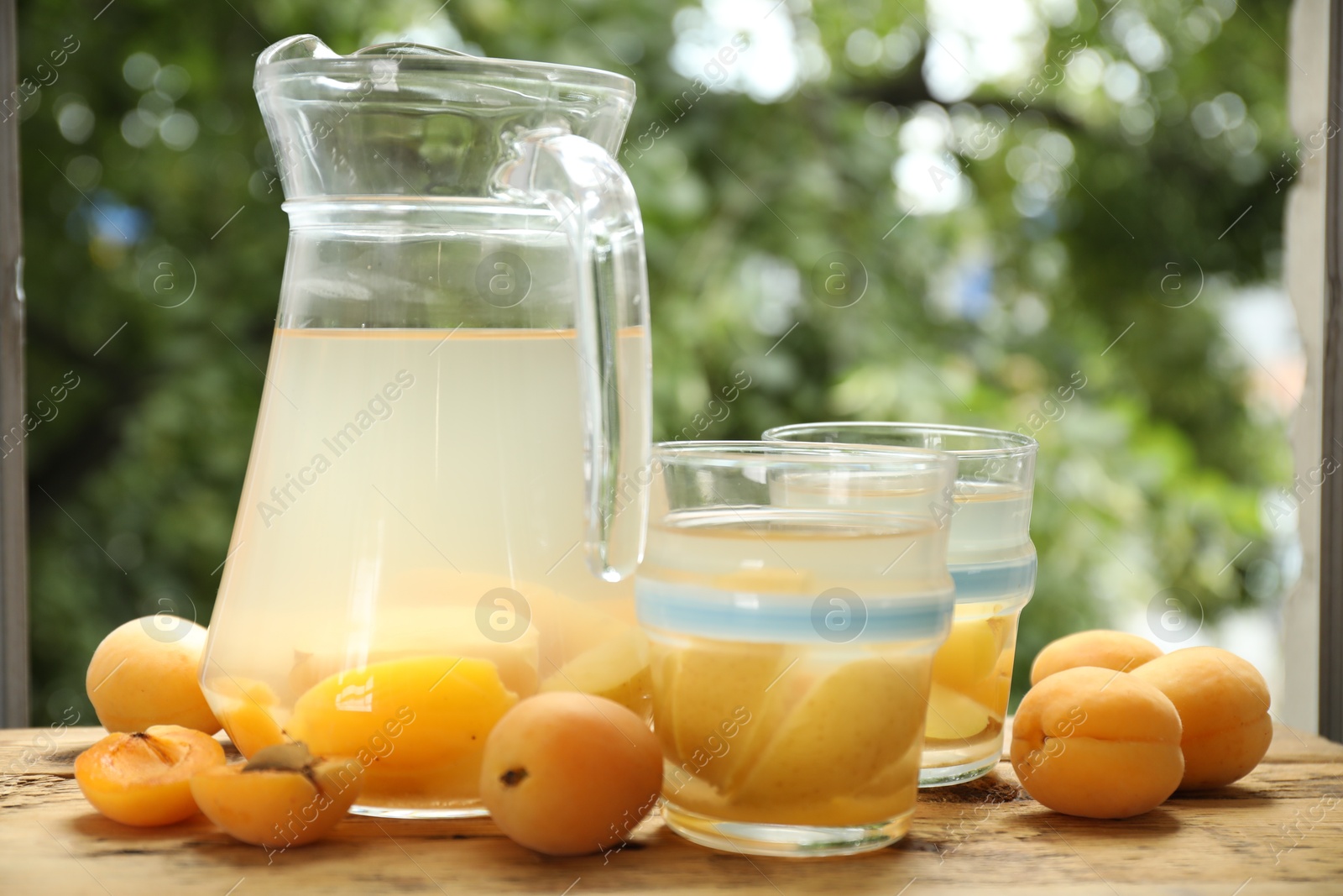 Photo of Tasty compot with apples in glasses, jug and fresh apricots on wooden table outdoors