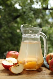 Photo of Tasty compot in glass jug and fresh apples on wooden table outdoors