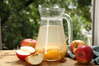 Photo of Tasty compot in glass jug and fresh apples on wooden table outdoors, closeup
