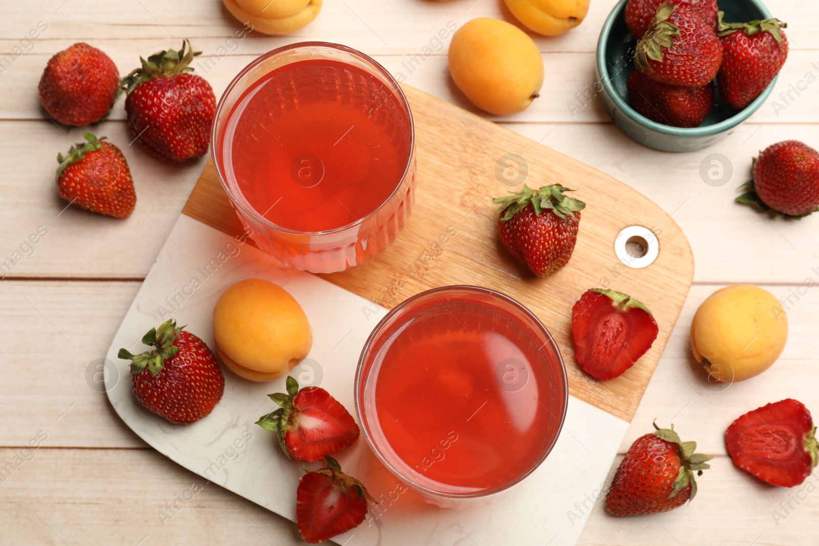 Photo of Tasty compot in glasses, fresh strawberries and apricots on wooden table, flat lay