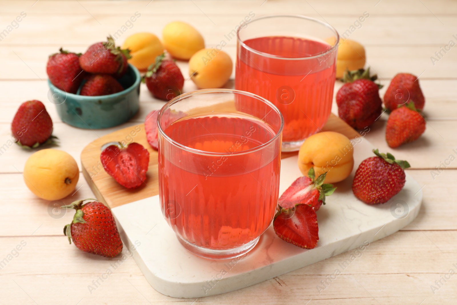 Photo of Tasty compot in glasses, fresh strawberries and apricots on wooden table, closeup