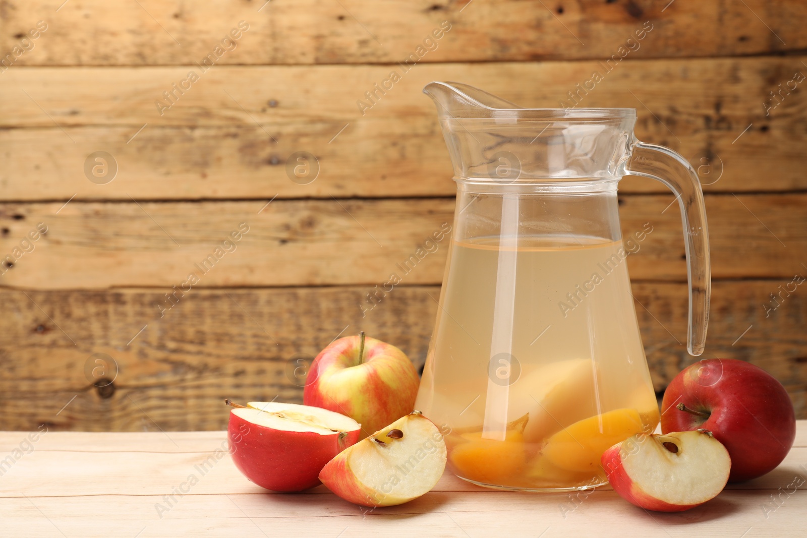 Photo of Tasty compot in glass jug and fresh apples on wooden table, space for text