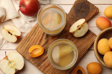 Photo of Tasty compot in glasses, fresh apples and apricots on wooden table, flat lay