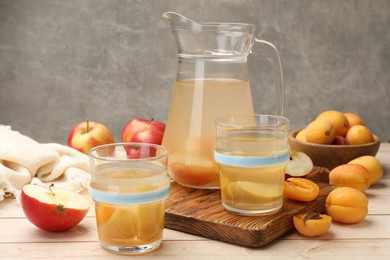 Photo of Tasty compot in glasses, jug, fresh apricots and apples on wooden table