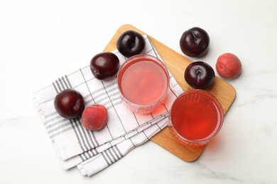 Photo of Tasty compot in glasses, plums and apricots on white marble table, flat lay