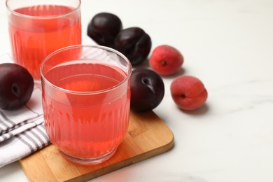Photo of Tasty compot in glasses, plums and apricots on white marble table, closeup. Space for text