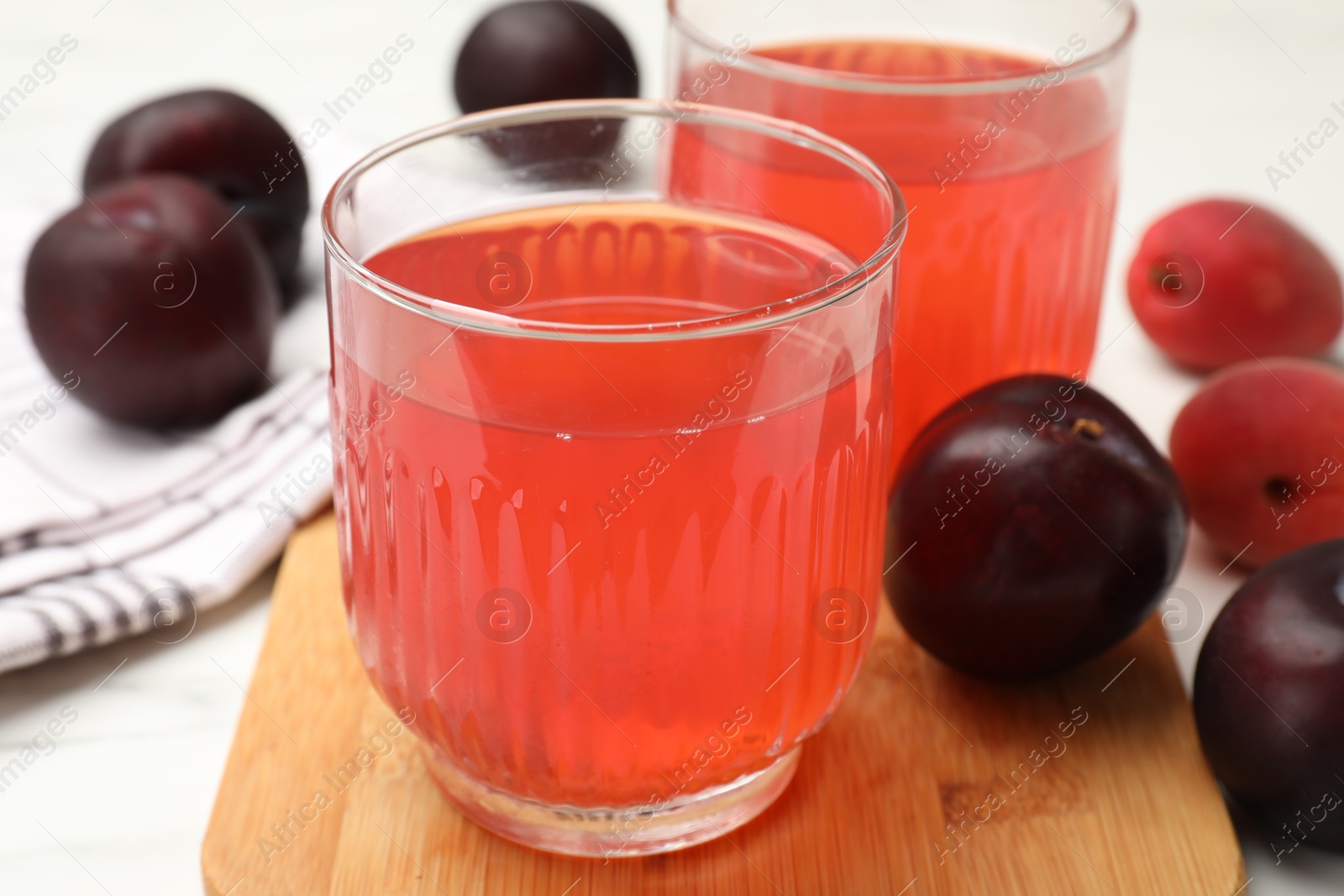 Photo of Tasty compot in glasses, plums and apricots on white marble table, closeup