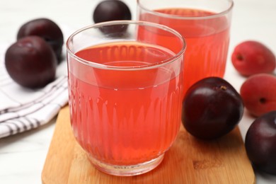 Photo of Tasty compot in glasses, plums and apricots on white marble table, closeup