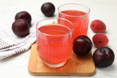 Photo of Tasty compot in glasses, plums and apricots on white marble table, closeup