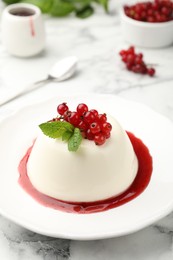Photo of Delicious panna cotta with red currants, sauce and mint on white marble table, closeup