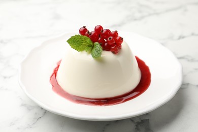 Photo of Delicious panna cotta with red currants, sauce and mint on white marble table, closeup